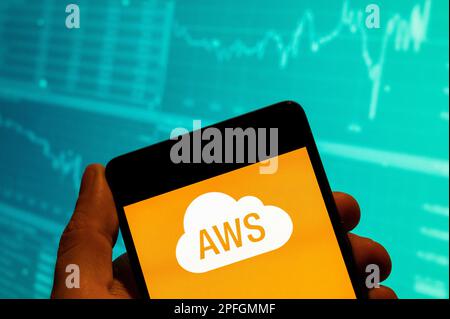 In this photo illustration, the American on-demand cloud computing platform owned by Amazon, Amazon Web Services AWS logo is seen displayed on a smartphone with an economic stock exchange index graph in the background. Stock Photo