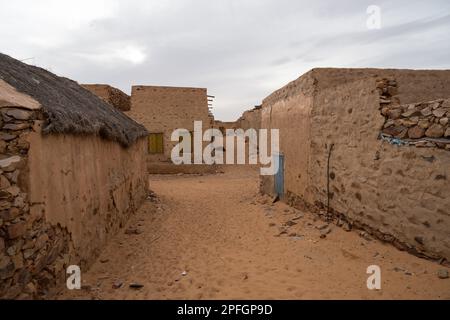 A narrow street in the ancient city of Chinguetti, Mauritania, lined with historic stone buildings, with the desert sands encroaching. Stock Photo