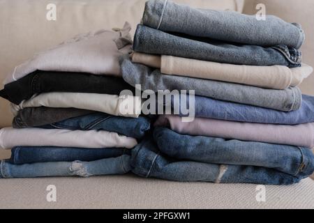 Denim pants, different colours of folded and stacked denim pants on a white sofa, denim fabric concept idea photo. Stock Photo