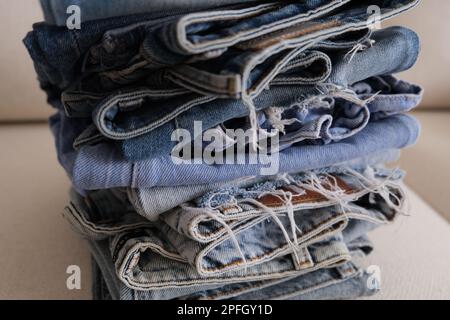 Folded denim jeans pants, stack of different shades of denim jeans on a white sofa. Folded denim pants in a row on a white armchair. Concept idea. Stock Photo