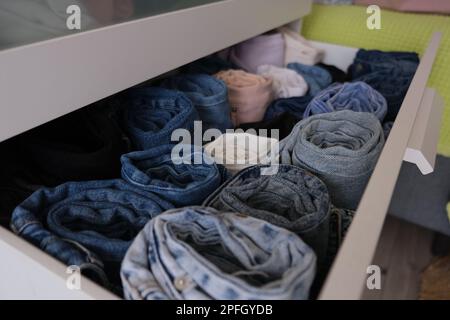 Drawer full of denim trousers, open drawer with folded denim jeans trousers indoors. Diagonally frame concept idea photo. Selective focus Stock Photo