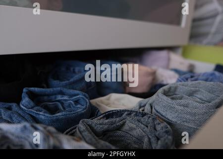 Drawer stack of denim clothes, fully open white drawer stack of folded denim clothes indoors, close up. Selective focus. Denim concept idea photo. Stock Photo