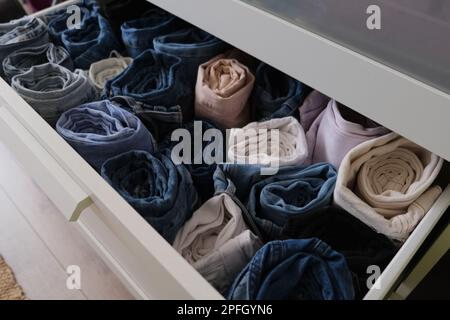 Drawer full of denim clothes, near open drawer with folded denim jeans clothes indoors. Diagonally frame concept idea photo. Stock Photo