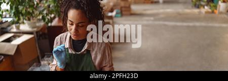 Woman florist wearing apron is taking notes during working day in floral studio Stock Photo