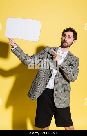 Charming guy in jacket pointing at empty speech bubble on yellow background,stock image Stock Photo