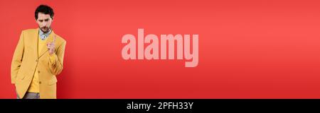 displeased model in stylish clothes pointing with finger on coral red background, banner,stock image Stock Photo