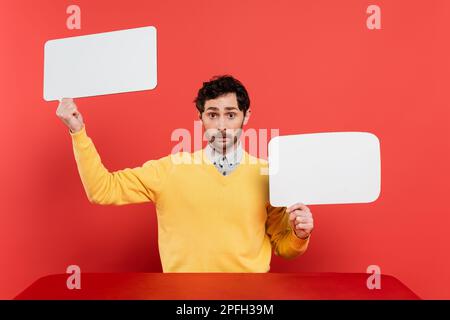 bearded man in yellow long sleeve jumper holding blank speech bubbles on red coral background,stock image Stock Photo