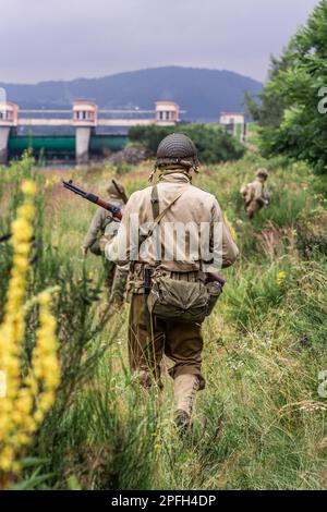 Porabka, Poland – July18, 2020 : Historical reconstruction. World War II american infantry  soldiers  patrol the area  in the tall grass. View from th Stock Photo