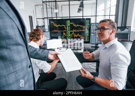 With documents. Team of stockbrokers works in modern office with many display screens Stock Photo