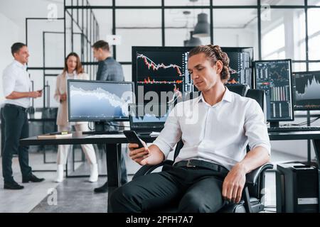 Ordinary office day. Team of stockbrokers works in indoors with many display screens Stock Photo