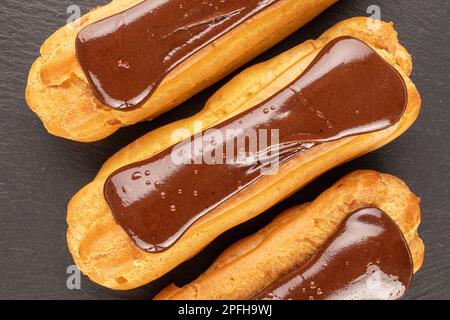 Three chocolate eclairs, close-up, on slate stone, top view. Stock Photo