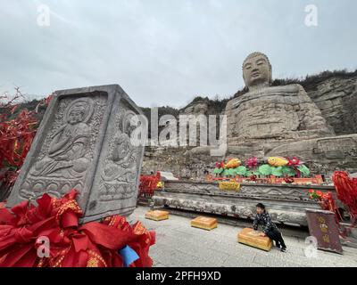A boy plays at the foot of the Mengshan Giant Buddha in the north peak of Mengshan Mountain in Taiyuan, capital city of China's Shanxi province, on March 11, 2023. According to the record, Mengshan Giant Buddha was originally built during the North Qi DynastyＡH50-577). The Buddha was rediscovered in 1980 census after it disappeared from the public eyes for several hundred years, with its head missing. From 2006 to 2008, people constructed a 12-meter-tall head for the statue and the site opened to the public in 2008.   11MAR23. SCMP/Simon Song Stock Photo