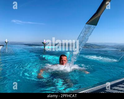 Man Enjoy Infinity Swimming Pool with Mountain and Lake Lucerne  View in a Sunny Day in Burgenstock, Nidwalden, Switzerland. Stock Photo