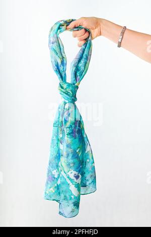 Female hand holding silk colourful hand painted tied scarf over grey background. Woman fashion, tying a scarf, wearing a scarves. Stylish ways to tie Stock Photo