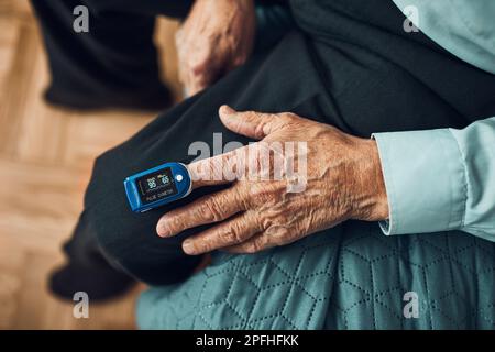 Senior man measuring the degree of oxygen saturation of the blood and heart rate at home using pulse oximeter. Home treatment of virus. Checking healt Stock Photo