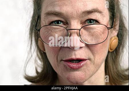 Close up portrait of a middle-age Caucasian woman wearing eyeglasses enlarge earings posing on a white background Stock Photo
