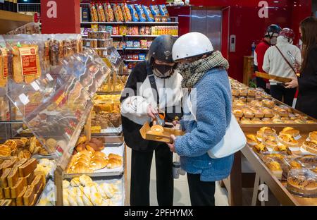 Two young Vietnamese women wearing motorcycle helmets select pastries in a bakery in Dalat, Vietnam. Stock Photo