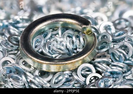 Big metal spring washer lying on heap of small stainless split washers blurry on background. Closeup of steel helical ring for screw and nut fastening. Stock Photo