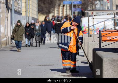 Cleaning street in a city, woman janitor with broom removes trash on crowd of people background. Work of housing and communal services in spring Stock Photo