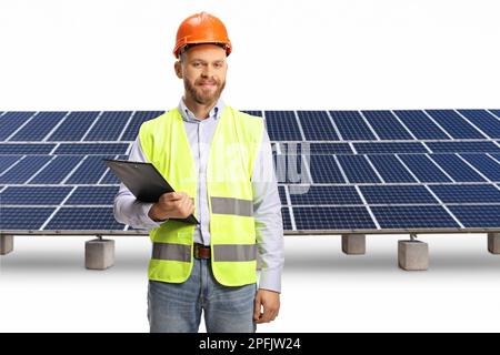 Young male engineer with a hardhat holding a clipboard in front of solar panels isolated on white background Stock Photo