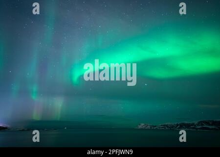 farbige, tanzende Aurora Borealis über der Insel vor Troms, Norwegen. wunderbare Nordlichter über dem Dorf Hillesøy. Polarlicht spiegelt sich im Meer Stock Photo