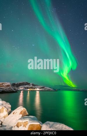 tanzende Nordlichter über dem Dorf Brensholmen auf der Insel Kvaløya. farbige Aurora Borealis spiegelt sich im Meer. Polarlicht in Troms, Norwegen Stock Photo