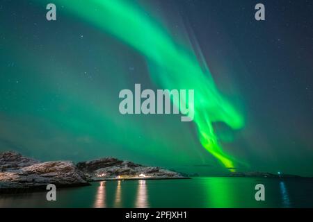 tanzende Nordlichter über dem Dorf Brensholmen auf der Insel Kvaløya. farbige Aurora Borealis spiegelt sich im Meer. Polarlicht in Troms, Norwegen Stock Photo