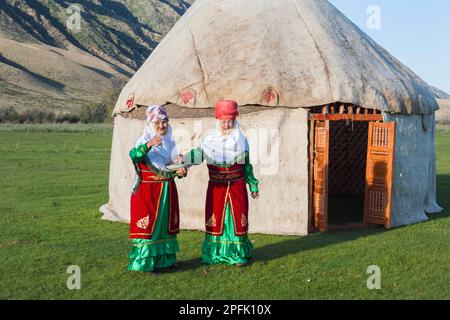 Two Kazakh woman in traditional dress in front of a yurt greeting guests with sweets, For editorial use only, Sati village, Tien Shan Mountains Stock Photo