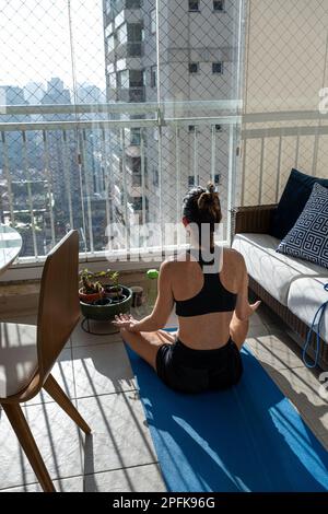 Brazilian woman, 42 years old, sitting in a yoga position, meditating and receiving sunlight vertical. Stock Photo