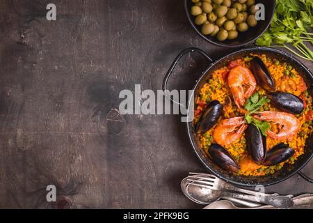 Paella background, space for text. Paella in black pan with saffron rice, peas, shrimps, mussels, squid, meat. Seafood paella, traditional spanish Stock Photo