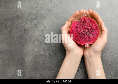 Woman holding fresh cut dragon fruit (pitahaya) on grey table, top view. Space for text Stock Photo