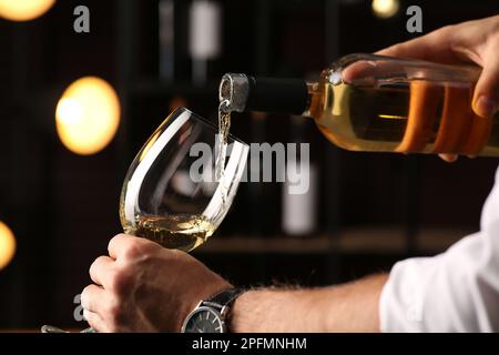 Man pouring white wine into glass indoors, closeup Stock Photo