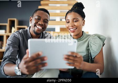 We compliment each other as teammates. two young businesspeople sitting together on a staircase in the office and using a digital tablet. Stock Photo