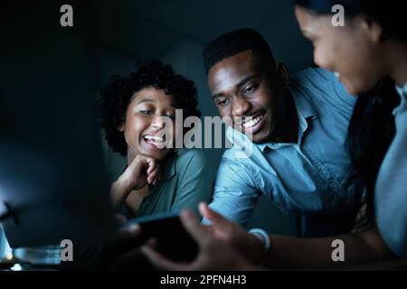 Creative minds are in constant motion. a group of young businesspeople using a smartphone and computer together during a late night at work. Stock Photo