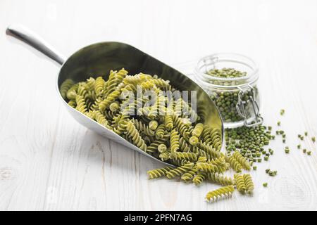 Mung bean fusilli pasta on a wooden background. Scoop with raw pasta and green mung bean. Gluten free pasta. Stock Photo