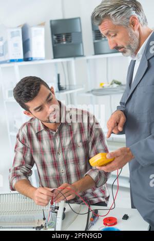 supervisor instructing apprentice using multimeter on electrical appliance Stock Photo