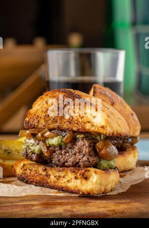 Caramelized onion burger with avocado sauce cut in half, with sauces and french fries on the side Stock Photo