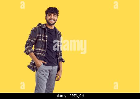 Portrait of carefree indian casual guy with beautiful smile near copy space on yellow background. Stock Photo
