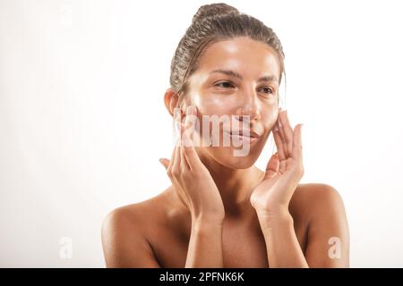 Beautiful girl smearing face cream on her skin at the studio on a white backround Stock Photo