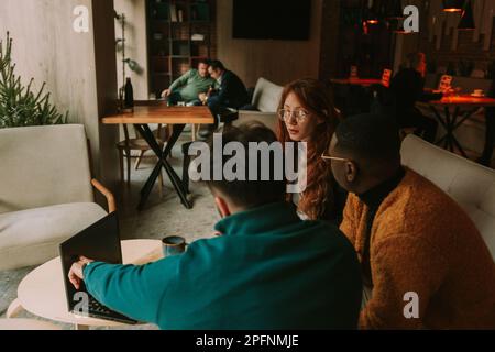 Multiracial coworkers discussing business while working remotely. Male person pointing at the lap top Stock Photo