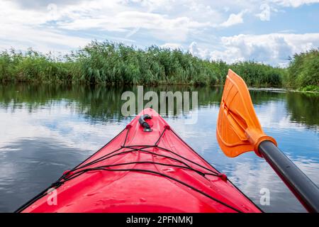 Kayaker point of view. Red kayak bow with a view on the river and rushes.   River kayaking concept. Active vacations in wild nature. Stock Photo