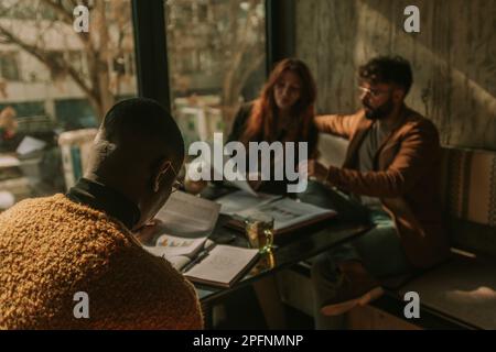 Back view shot of black businessman reading financial statistics and teamwork results while his white colleagues are working together at the other sid Stock Photo