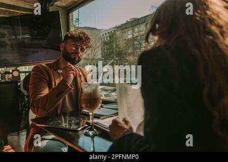 Good looking male person listening carefully to his redhead female colleague and writing notes down in a notebook while she is reading important stats Stock Photo