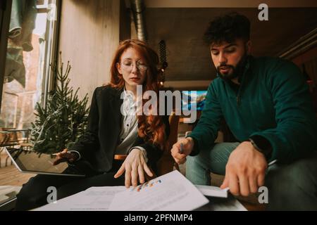 Lowe angle view photo of lovely business coworkers making a sales profit report for the month. They are working remote, at coffee bar Stock Photo