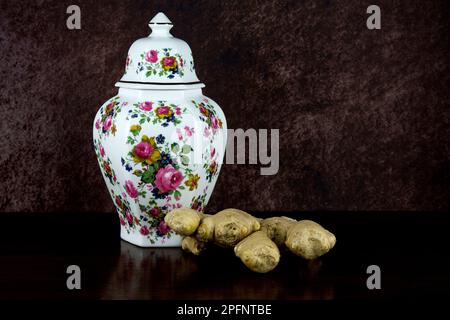 Large ceramic ginger jar and fresh ginger on a polished wooden table top Stock Photo