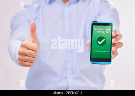 Man, hands and phone with thumbs up for transaction approval against a white studio background. Hand of male showing thumb emoji, yes sign or like for Stock Photo