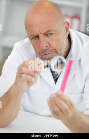 concentrated senior scientist chemists hold magnifying glass in lab Stock Photo