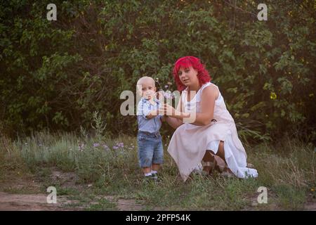 Little boy give bouquet of wild flowers to mother with love. Mothers day concept. Young diversity woman with pink hair walks with child in nature in t Stock Photo