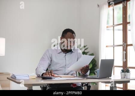 Focused african businessman holding documents looking at laptop doing research. business financial analyst concept Stock Photo