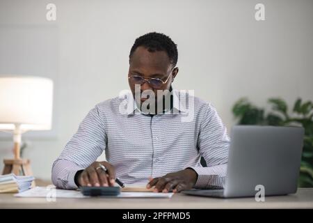 Focused african businessman holding documents looking at laptop doing research. business financial analyst concept Stock Photo